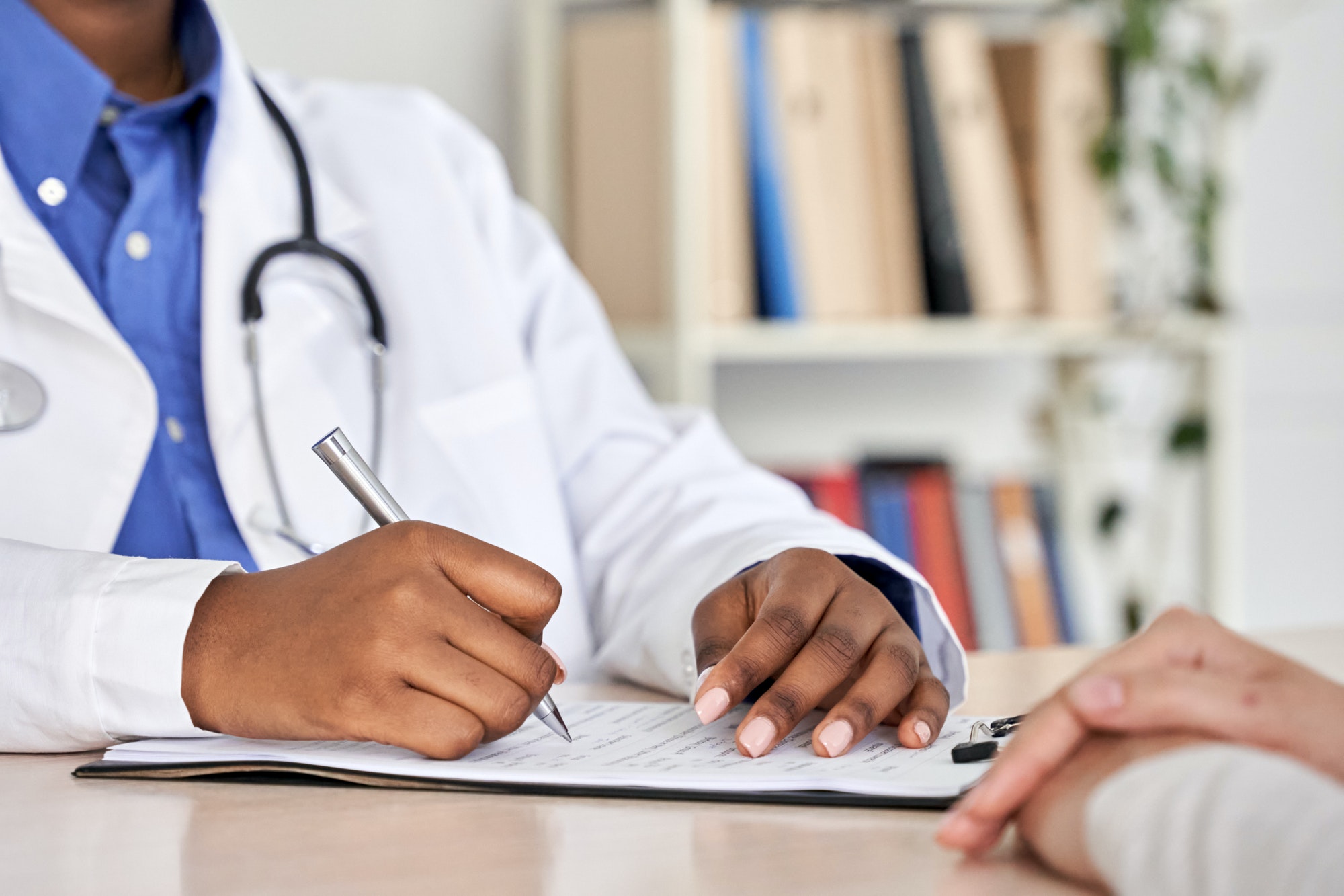 African black doctor consult woman patient filling medical form at appointment.